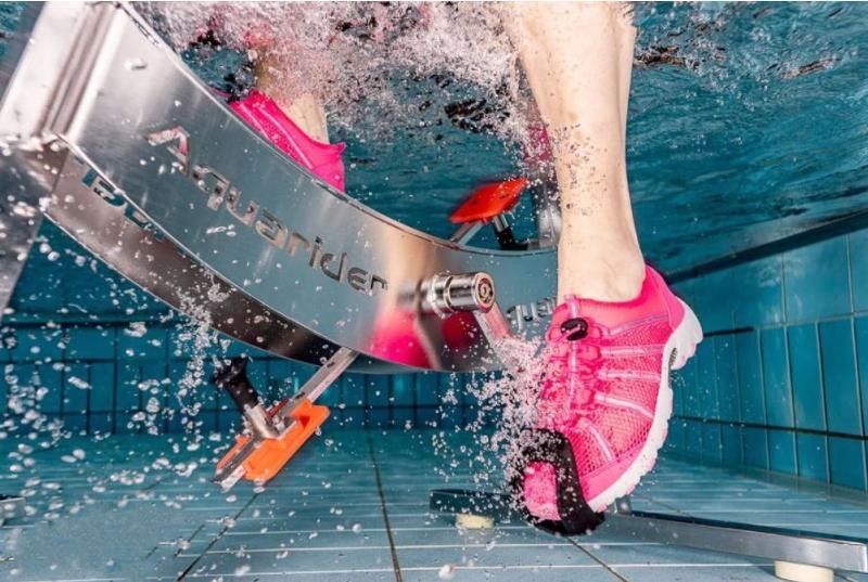 Hier sieht man den unteren Teil eines Aquariderfahrrades wie jemand mit rosa Schuhen es fährt