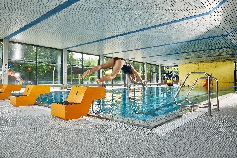 Hallenbad Hier sieht man die Schwimmhalle von innen und eine Person Spring mit einem Köpfer in das Wasser