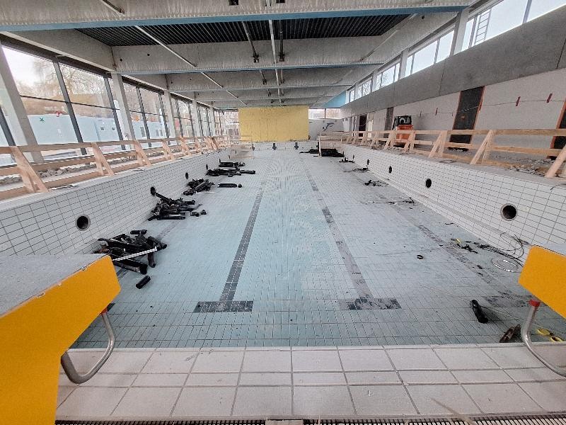 Halle ohne Decke und kaputte Fliesen Hier sieht man das leere Becken mit einer Absturtzsicherung und der fehlenden Deckenverkleidung und Rohren im Becken